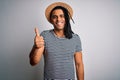 Young african american man with dreadlocks on vacation wearing striped t-shirt and hat doing happy thumbs up gesture with hand Royalty Free Stock Photo