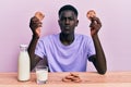 Young african american man drinking a glass of fresh milk with cookies making fish face with mouth and squinting eyes, crazy and