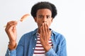 Young african american man eating nigiri using chopsticks over isolated white background cover mouth with hand shocked with shame