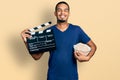 Young african american man eating popcorn holding film clapboard smiling with a happy and cool smile on face Royalty Free Stock Photo