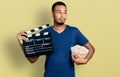 Young african american man eating popcorn holding film clapboard smiling looking to the side and staring away thinking Royalty Free Stock Photo