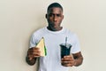 Young african american man eating sandwich and drinking soda making fish face with mouth and squinting eyes, crazy and comical Royalty Free Stock Photo