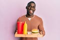 Young african american man eating a tasty classic burger and soda winking looking at the camera with sexy expression, cheerful and