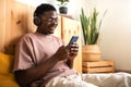 Young african american man with glasses relaxing at home listening to music with headphones while using mobile phone. Royalty Free Stock Photo