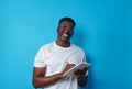 A young African-American man with glasses writes down information in a notebook on a blue background Royalty Free Stock Photo