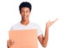 Young african american man holding banner cardboard celebrating victory with happy smile and winner expression with raised hands Royalty Free Stock Photo