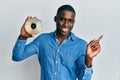 Young african american man holding compact disc smiling happy pointing with hand and finger to the side Royalty Free Stock Photo