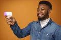 Young african american man holding contactless thermometer against yellow background