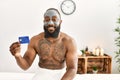 Young african american man holding credit card having skin facial mask treatment at beauty center