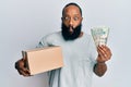 Young african american man holding delivery box and usa dollars banknotes making fish face with mouth and squinting eyes, crazy Royalty Free Stock Photo