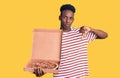 Young african american man holding delivery pizza box with angry face, negative sign showing dislike with thumbs down, rejection Royalty Free Stock Photo