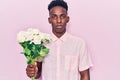 Young african american man holding flowers thinking attitude and sober expression looking self confident