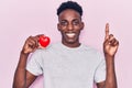 Young african american man holding heart smiling with an idea or question pointing finger with happy face, number one Royalty Free Stock Photo