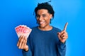 Young african american man holding 20 israel shekels banknotes smiling happy pointing with hand and finger to the side