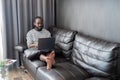 Young African American man holding laptop relaxing sitting on sofa working remote at home Royalty Free Stock Photo