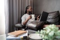 Young African American man holding laptop relaxing sitting on sofa working remote at home Royalty Free Stock Photo