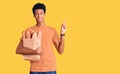 Young african american man holding paper bag with bread with a big smile on face, pointing with hand finger to the side looking at Royalty Free Stock Photo