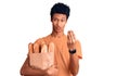 Young african american man holding paper bag with bread doing money gesture with hands, asking for salary payment, millionaire Royalty Free Stock Photo