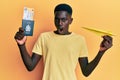 Young african american man holding paper plane and passport in shock face, looking skeptical and sarcastic, surprised with open Royalty Free Stock Photo