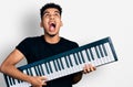 Young african american man holding piano keyboard angry and mad screaming frustrated and furious, shouting with anger looking up Royalty Free Stock Photo