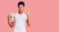 Young african american man holding popcorn doing ok sign with fingers, smiling friendly gesturing excellent symbol Royalty Free Stock Photo
