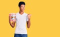 Young african american man holding popcorn pointing thumb up to the side smiling happy with open mouth Royalty Free Stock Photo