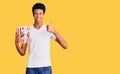 Young african american man holding popcorn smiling happy and positive, thumb up doing excellent and approval sign Royalty Free Stock Photo