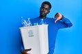 Young african american man holding recycling wastebasket with plastic bottles with angry face, negative sign showing dislike with Royalty Free Stock Photo