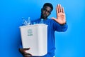 Young african american man holding recycling wastebasket with plastic bottles with open hand doing stop sign with serious and Royalty Free Stock Photo