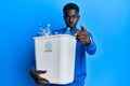 Young african american man holding recycling wastebasket with plastic bottles pointing with finger to the camera and to you, Royalty Free Stock Photo