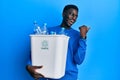 Young african american man holding recycling wastebasket with plastic bottles pointing thumb up to the side smiling happy with Royalty Free Stock Photo
