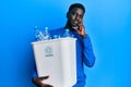 Young african american man holding recycling wastebasket with plastic bottles serious face thinking about question with hand on Royalty Free Stock Photo