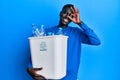 Young african american man holding recycling wastebasket with plastic bottles smiling happy doing ok sign with hand on eye looking Royalty Free Stock Photo