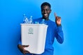Young african american man holding recycling wastebasket with plastic bottles surprised with an idea or question pointing finger Royalty Free Stock Photo
