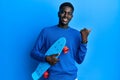 Young african american man holding skate pointing thumb up to the side smiling happy with open mouth Royalty Free Stock Photo