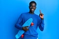 Young african american man holding skate smiling with an idea or question pointing finger with happy face, number one Royalty Free Stock Photo