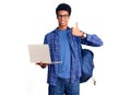 Young african american man holding student backpack using laptop smiling happy and positive, thumb up doing excellent and approval Royalty Free Stock Photo