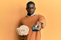 Young african american man holding television remote control eating popcorn skeptic and nervous, frowning upset because of problem