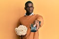 Young african american man holding television remote control eating popcorn smiling looking to the side and staring away thinking Royalty Free Stock Photo