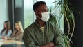 Young african american man in medical mask look at camera at modern office. Businessman at office in quarantine Royalty Free Stock Photo