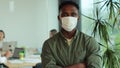 Young african american man in medical mask look at camera at modern office. Businessman at office in quarantine Royalty Free Stock Photo