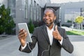 A young African American man near the office in headphones and talking on a video call on a tablet Royalty Free Stock Photo