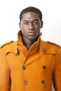 Young African American man in orange trench coat standing against white background