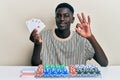 Young african american man playing poker holding cards doing ok sign with fingers, smiling friendly gesturing excellent symbol Royalty Free Stock Photo