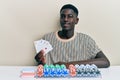 Young african american man playing poker holding cards looking positive and happy standing and smiling with a confident smile Royalty Free Stock Photo