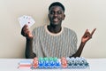 Young african american man playing poker holding cards smiling happy pointing with hand and finger to the side Royalty Free Stock Photo