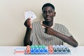 Young african american man playing poker holding cards smiling happy pointing with hand and finger Royalty Free Stock Photo