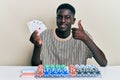 Young african american man playing poker holding cards smiling happy and positive, thumb up doing excellent and approval sign Royalty Free Stock Photo