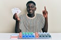 Young african american man playing poker holding cards smiling with an idea or question pointing finger with happy face, number Royalty Free Stock Photo