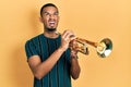 Young african american man playing trumpet angry and mad screaming frustrated and furious, shouting with anger looking up Royalty Free Stock Photo